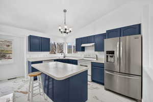 Kitchen with blue cabinets, stainless steel fridge with ice dispenser, vaulted ceiling, hanging light fixtures, and light marble finish flooring