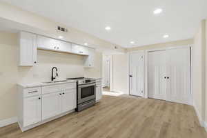 Kitchen with white cabinetry, stainless steel range with electric stovetop, recessed lighting, light wood-type flooring, and light stone countertops