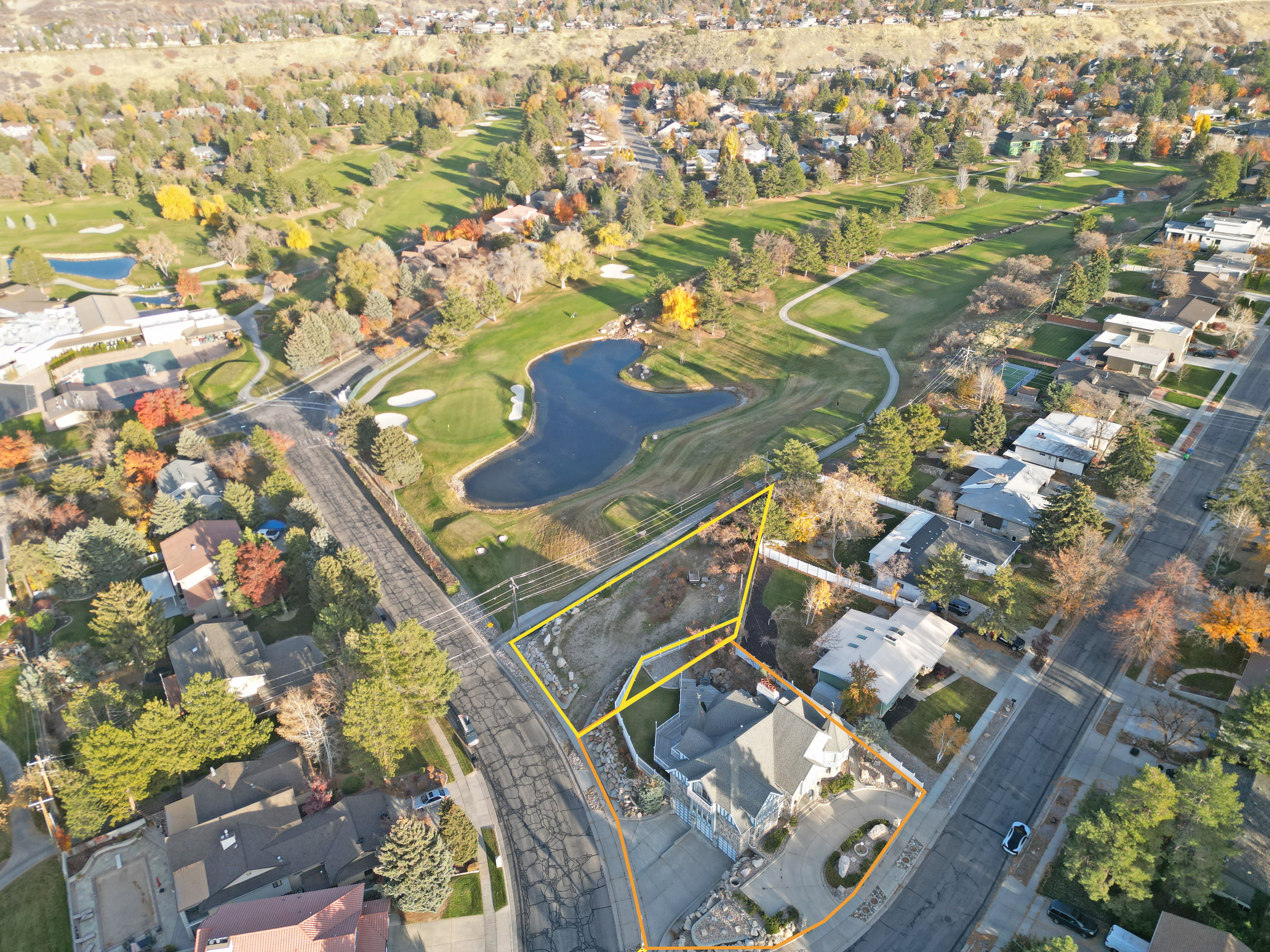Aerial perspective showcasing a residential property with a multi-level home and mature landscaping, bordering a golf course featuring manicured greens and water features