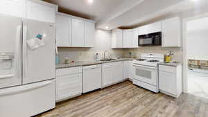Kitchen with white appliances, white cabinetry, light wood-style floors, light stone countertops, and recessed lighting