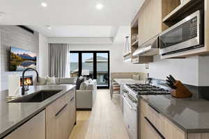 Kitchen with open shelves, stainless steel appliances, light brown cabinetry, and dark stone countertops