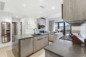 Kitchen with modern cabinets, dark stone counters, light wood finished floors, a kitchen island with sink, and stainless steel dishwasher