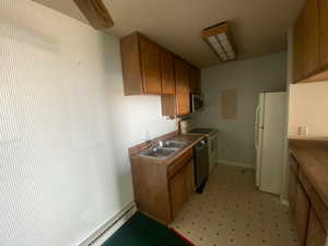 Kitchen with light floors, stainless steel appliances, brown cabinets, light countertops, and a baseboard radiator