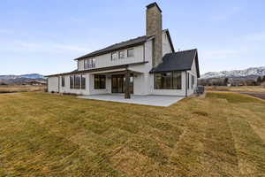 Rear view of property featuring a mountain view, a patio area, a yard, and a chimney