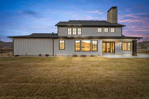 Rear view of property with a yard, a patio, a chimney, and board and batten siding