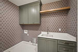 Laundry room featuring wallpapered walls, washer hookup, cabinet space, and a textured ceiling