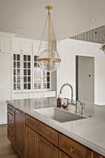 Kitchen with brown cabinetry, decorative light fixtures, light stone counters, a textured ceiling, and glass insert cabinets