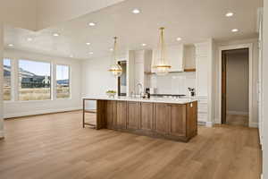 Kitchen with brown cabinets, an island with sink, white cabinets, a breakfast bar, and recessed lighting