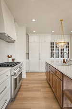 Kitchen featuring white cabinets, brown cabinetry, range with two ovens, light wood-type flooring, and custom range hood