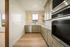 Kitchen with stainless steel appliances, decorative backsplash, light wood-style floors, open shelves, and gray cabinetry