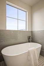 Full bath featuring a soaking tub, tile walls, and a wainscoted wall