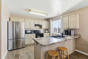 Kitchen featuring freestanding refrigerator, black range with electric cooktop, a peninsula, light countertops, and a breakfast bar area