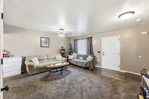 Living room featuring a textured ceiling, dark colored carpet, and a ceiling fan