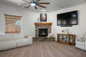 Carpeted living room with a ceiling fan and a stone fireplace