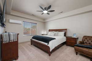 Bedroom featuring a raised ceiling, carpet flooring, a ceiling fan, and a wall mounted air conditioner