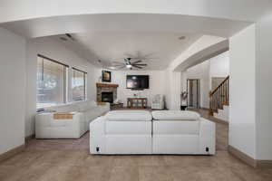 Living area with ceiling fan, arched walkways, a fireplace, stairway, and light tile patterned flooring