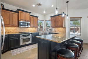 Kitchen featuring light stone countertops, stainless steel appliances, hanging light fixtures, a breakfast bar, and light tile patterned floors