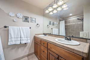 Bathroom with double vanity, a tile shower, and a chandelier
