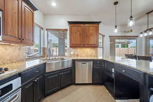 Kitchen with light stone counters, appliances with stainless steel finishes, hanging light fixtures, and recessed lighting