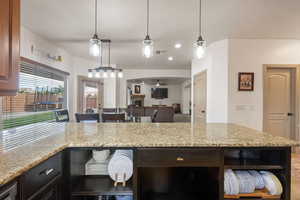 Kitchen featuring light stone countertops, a warm lit fireplace, hanging light fixtures, open shelves, and recessed lighting