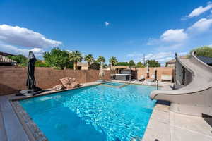 View of pool featuring a water slide, a fenced backyard, an in-ground hot tub, and a patio