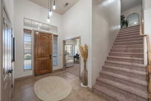 Foyer with a high ceiling, stairway, light tile patterned flooring, and healthy amount of natural light