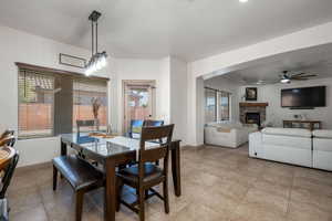 Dining space featuring a fireplace, ceiling fan, light tile patterned flooring, and a chandelier