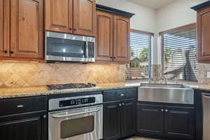 Kitchen featuring appliances with stainless steel finishes, light stone counters, decorative backsplash, and dark cabinetry