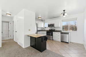 Kitchen featuring butcher block countertops, appliances with stainless steel finishes, white cabinets, light colored carpet, and light tile patterned floors