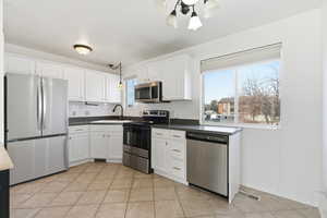 Kitchen with stainless steel appliances, decorative light fixtures, white cabinets, backsplash, and light tile patterned floors