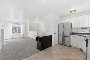 Kitchen with appliances with stainless steel finishes, white cabinetry, open floor plan, a chandelier, and light carpet