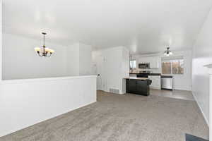 Kitchen featuring a chandelier, light colored carpet, white cabinetry, pendant lighting, and stainless steel appliances