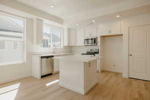 Kitchen with white cabinets, light countertops, appliances with stainless steel finishes, a center island, and recessed lighting