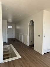Spare room featuring dark wood-style flooring, arched walkways, a textured ceiling, a decorative wall, and a wainscoted wall