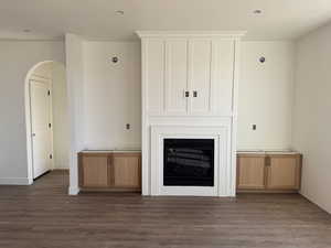 Unfurnished living room with arched walkways, a glass covered fireplace, and dark wood-type flooring
