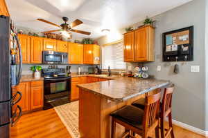 Kitchen with stainless steel appliances, a breakfast bar area, a peninsula, brown cabinetry, and light wood-style floors