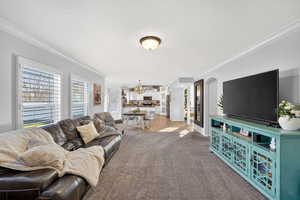 Carpeted living room featuring ornamental molding and a chandelier