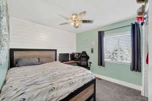 Bedroom featuring an accent wall, wooden walls, dark carpet, and ceiling fan