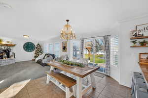 Dining room with healthy amount of natural light, light tile patterned flooring, ornamental molding, a stone fireplace, and a chandelier