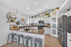 Kitchen with white cabinetry, stainless steel appliances, lofted ceiling, a peninsula, and light tile patterned floors