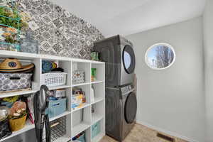 Laundry room featuring stacked washing machine and dryer and baseboards