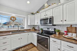 Kitchen with dark countertops, stainless steel appliances, white cabinets, lofted ceiling, and decorative backsplash