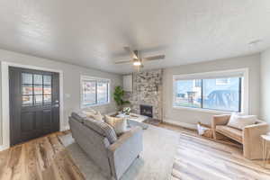 Living room featuring a textured ceiling, ceiling fan, a fireplace, healthy amount of natural light, and light wood-style flooring