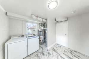 Washroom with concrete block wall, washer and dryer, secured water heater, and light marble finish floors