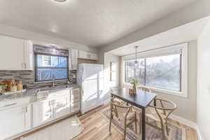 Kitchen with backsplash, white cabinets, new refrigerator, light stone countertops, and light wood-style floors