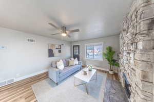 Living area with wood finished floors, a ceiling fan, and a stone fireplace