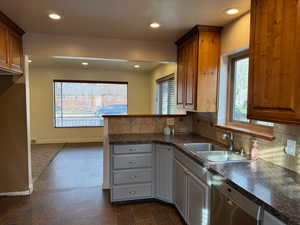 Kitchen featuring a peninsula, recessed lighting, dark countertops, stainless steel dishwasher, and tasteful backsplash