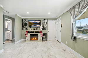 Living area with a glass covered fireplace, light marble finish floors, crown molding, and recessed lighting