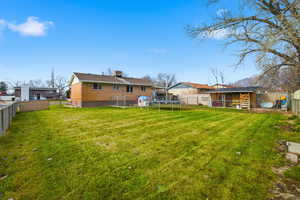 Back of property featuring a fenced backyard, a trampoline, a chimney, and brick siding