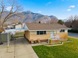 View of front of home with brick siding, roof with shingles, a front yard, and a mountain view